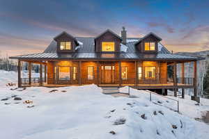 Snow covered house featuring covered porch, faux log siding, a metal roof, and a chimney
