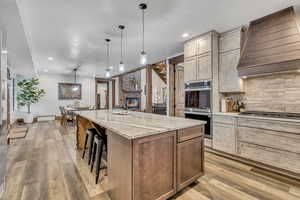 Kitchen with appliances with stainless steel finishes, custom exhaust hood, light stone counters, a kitchen breakfast bar, and a large fireplace