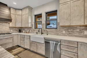 Kitchen featuring light brown cabinetry, stainless steel appliances, custom exhaust hood, light wood-style floors, and decorative backsplash