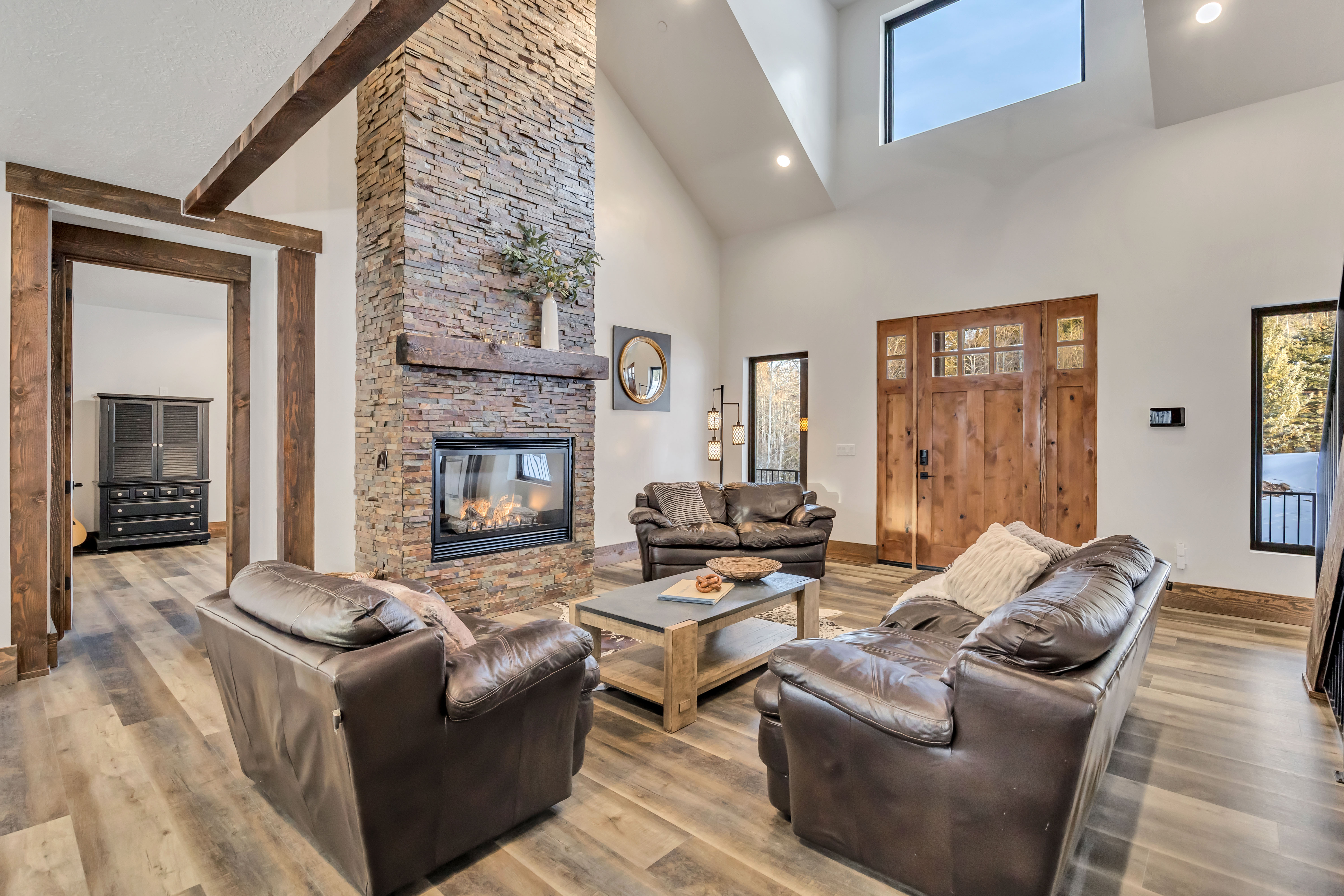 Living area with a stone fireplace, wood finished floors, recessed lighting, and a towering ceiling