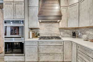 Kitchen with stainless steel appliances, custom exhaust hood, light brown cabinets, and tasteful backsplash