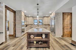 Kitchen featuring light brown cabinets, light stone countertops, open shelves, pendant lighting, and appliances with stainless steel finishes