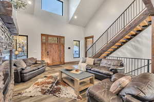 Living room with wood finished floors, a stone fireplace, stairway, a high ceiling, and recessed lighting