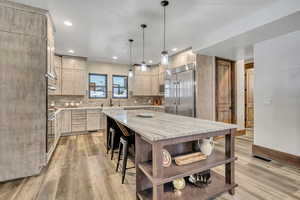 Kitchen with light brown cabinetry, pendant lighting, light stone counters, a center island, and stainless steel appliances