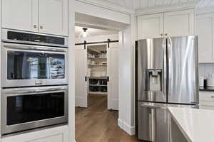 Kitchen with appliances with stainless steel finishes, white cabinetry, a barn door, dark wood finished floors, and dark stone countertops