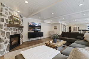 Living room featuring wood finished floors, a stone fireplace, beamed ceiling, and recessed lighting
