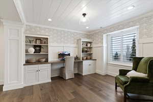 Home office featuring wallpapered walls, built in desk, a wainscoted wall, dark wood-type flooring, and ornamental molding