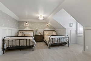 Bedroom featuring a decorative wall, wallpapered walls, a wainscoted wall, vaulted ceiling, and light colored carpet