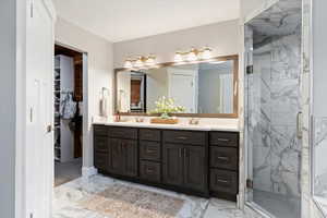 Bathroom with double vanity, a marble finish shower, a walk in closet, and light marble finish flooring