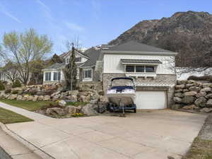 View of front of home with stone siding, driveway, an attached garage, and board and batten siding