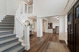 Foyer entrance with stairway, dark wood-style floors, recessed lighting, decorative columns, and a towering ceiling
