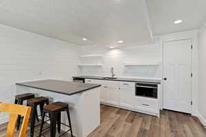 Kitchen with white cabinets, light wood-style floors, a kitchen breakfast bar, dark countertops, and a textured ceiling