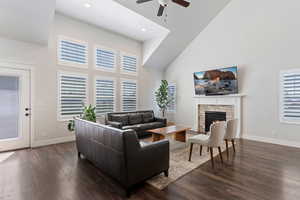Living room with a high ceiling, dark wood-type flooring, a ceiling fan, and a lit fireplace
