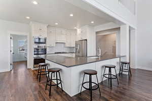 Kitchen with white cabinets, a peninsula, dark wood-style floors, appliances with stainless steel finishes, and recessed lighting