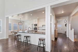 Kitchen with white cabinetry, dark wood finished floors, backsplash, a breakfast bar, and a chandelier