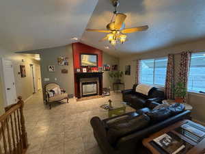 Tiled living area with a glass covered fireplace, a textured ceiling, vaulted ceiling, and ceiling fan