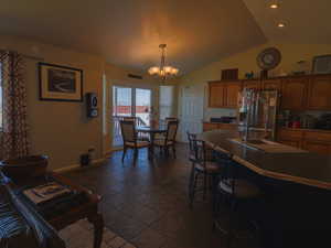 Kitchen with wood finish cabinets, dark countertops, stainless steel refrigerator with ice dispenser, vaulted ceiling, and a chandelier
