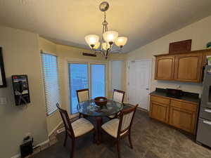 Dining room with a textured ceiling, vaulted ceiling, and a chandelier