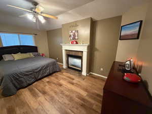 Bedroom with hardwood / wood-style floors, a textured ceiling, a tiled fireplace, and a ceiling fan