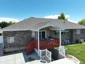 View of front facade with brick siding, a shingled roof, a patio area, a wooden deck, and a front lawn