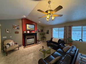 Tiled living area featuring a textured ceiling, lofted ceiling, a ceiling fan, and a tile fireplace