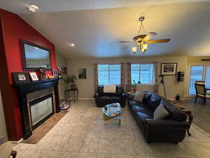 Living room with a glass covered fireplace, a textured ceiling, ceiling fan, lofted ceiling, and light tile patterned floors