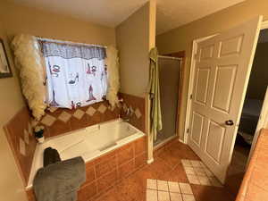 Bathroom with a stall shower, a textured ceiling, a garden tub, and light tile patterned floors