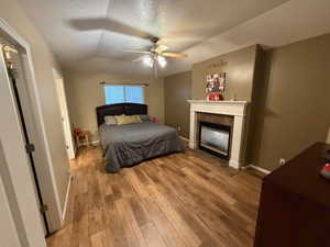 Bedroom featuring a textured ceiling, wood-type flooring, vaulted ceiling, ceiling fan, and a tiled fireplace