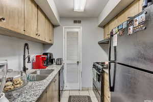 Kitchen with black appliances, light brown cabinets, light stone counters, light tile patterned floors, and under cabinet range hood