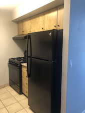 Kitchen with black appliances, extractor fan, light tile patterned floors, and light brown cabinets