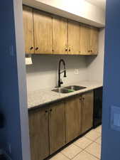 Kitchen featuring light stone counters, black dishwasher, light tile patterned floors, and brown cabinetry