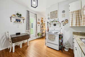 Kitchen featuring electric range, open shelves, light wood-type flooring, white cabinets, and light stone counters