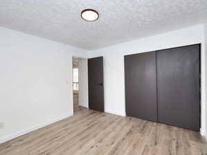 Unit #1- Unfurnished bedroom with a closet, a textured ceiling, and light wood-style flooring
