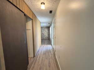 Unit #7-Corridor with brick wall, wood finished floors, and a textured ceiling
