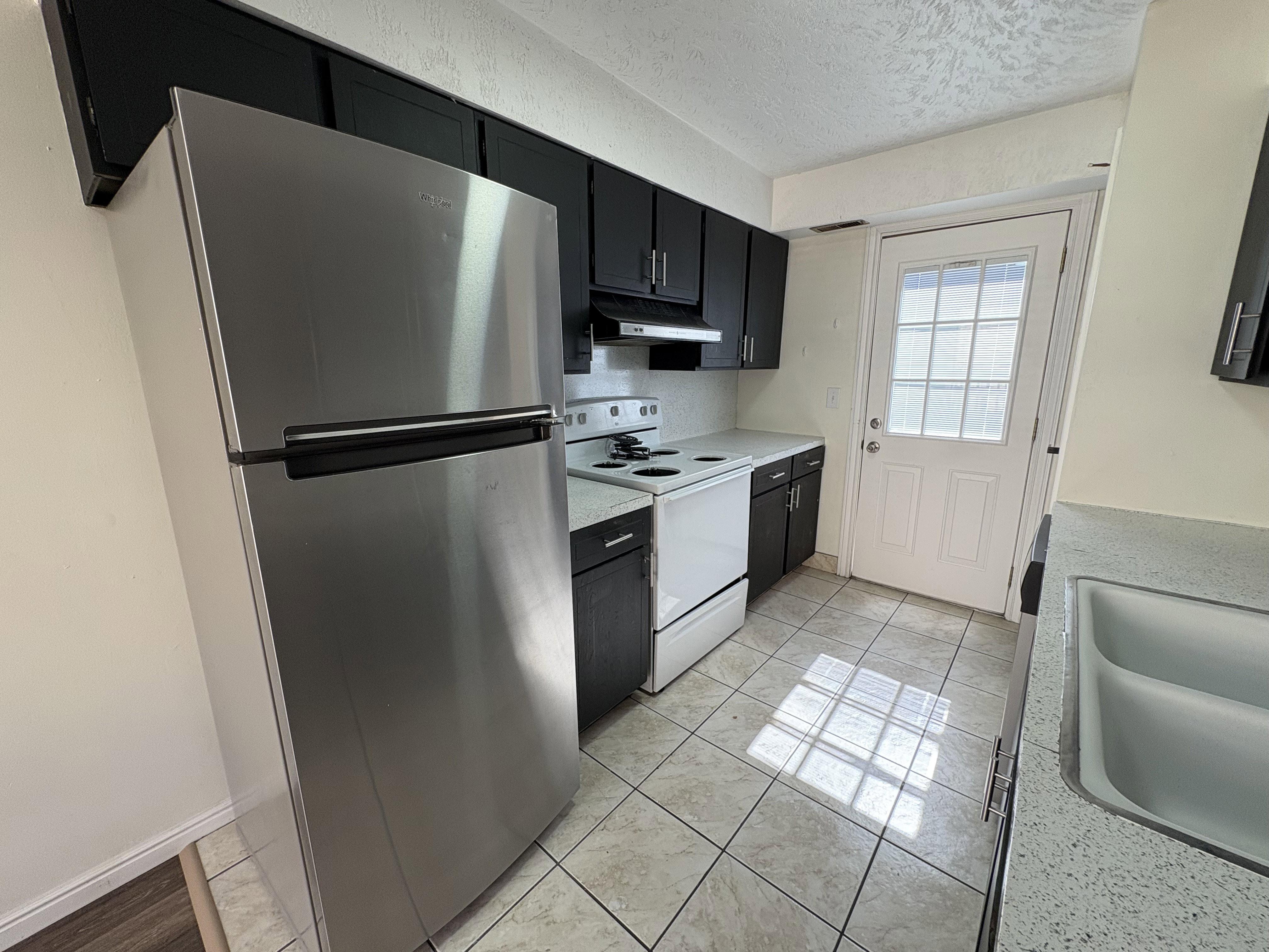 Unit #8- Kitchen with dark cabinetry, white range with electric stovetop, freestanding refrigerator, light countertops, and a textured ceiling