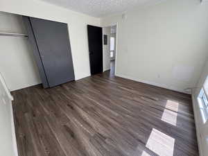 Unit #8- Unfurnished bedroom featuring a textured ceiling, dark wood-style flooring, and a closet