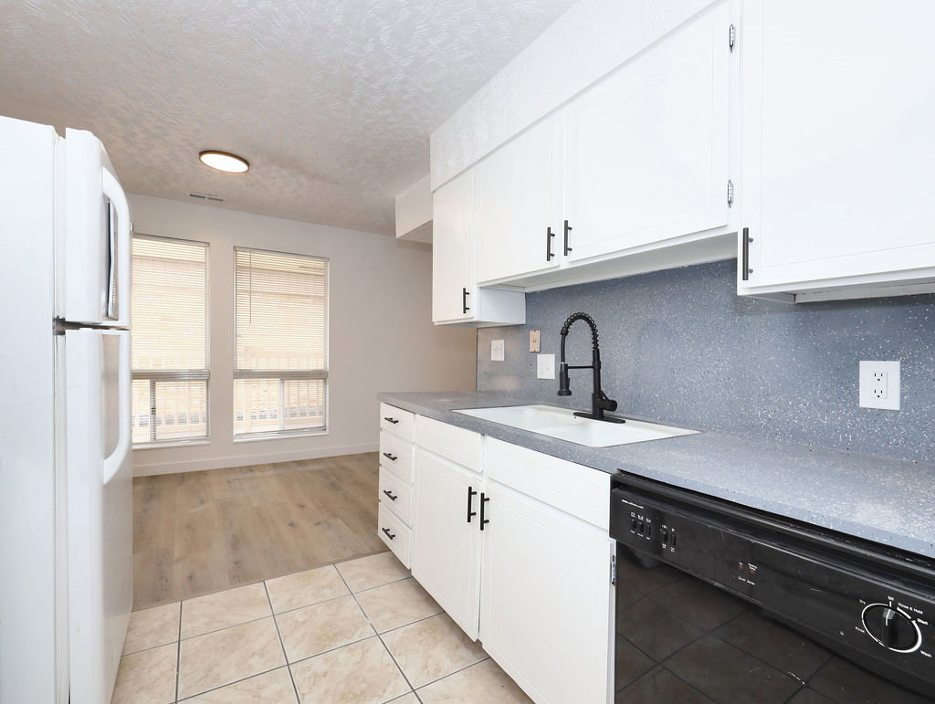 Unit #1- Kitchen with freestanding refrigerator, black dishwasher, a textured ceiling, backsplash, and light tile patterned floors