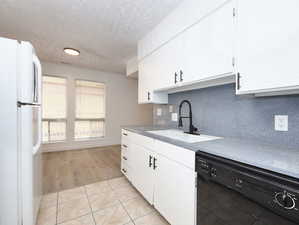 Unit #1- Kitchen with freestanding refrigerator, black dishwasher, a textured ceiling, backsplash, and light tile patterned floors