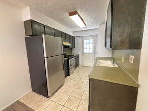 Unit #7- Kitchen with stainless steel appliances, a textured ceiling, light countertops, under cabinet range hood, and light tile patterned floors