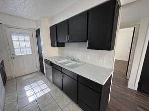 Unit #8- Kitchen featuring dark cabinetry, backsplash, dishwasher, a textured ceiling, and light stone countertops