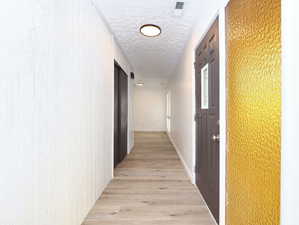 Unit #1- Corridor with light wood-type flooring and a textured ceiling