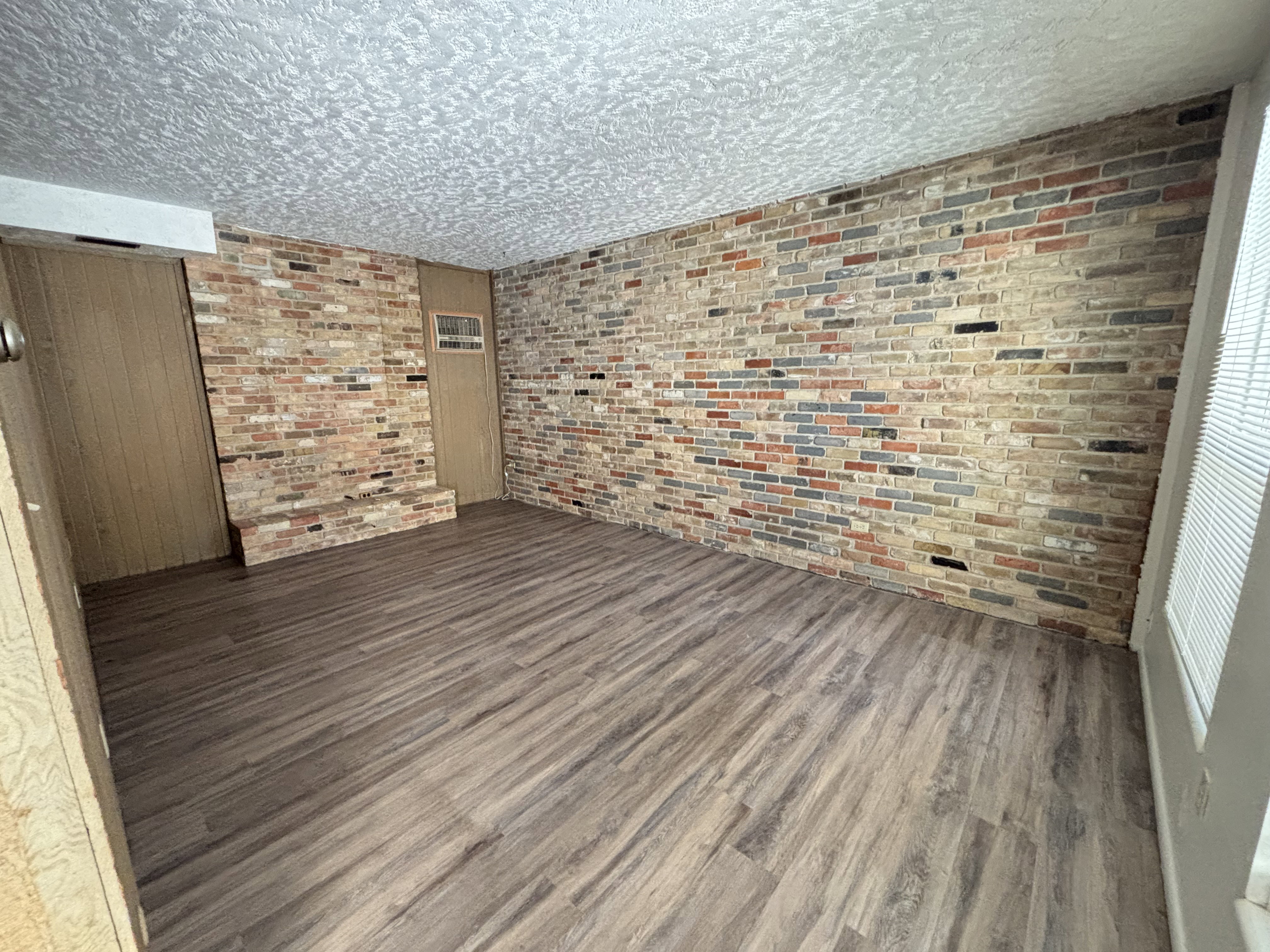 Unit #7-Unfurnished room featuring wood finished floors and brick wall