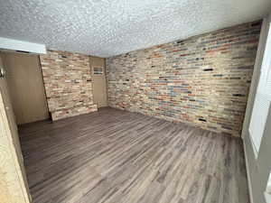 Unit #7-Unfurnished room featuring wood finished floors and brick wall