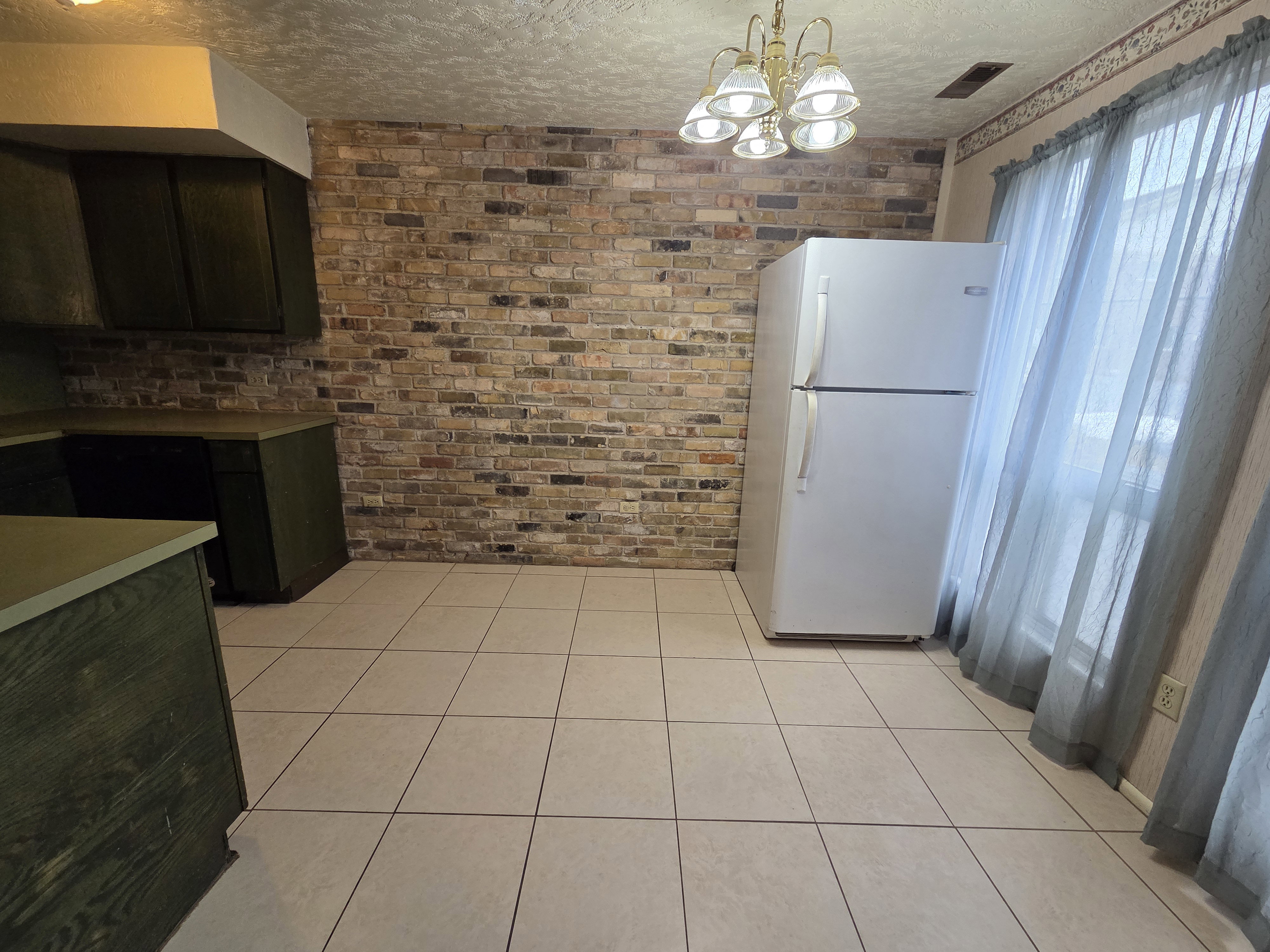 Unit #2- Kitchen with freestanding refrigerator, a textured ceiling, light tile patterned flooring, brick wall, and a chandelier