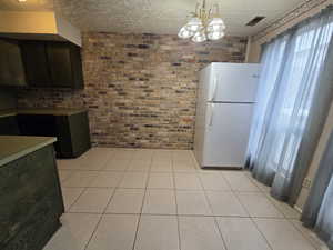 Unit #2- Kitchen with freestanding refrigerator, a textured ceiling, light tile patterned flooring, brick wall, and a chandelier