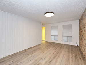 Unit #1- Empty room with light wood-style floors, a textured ceiling, and brick wall