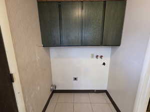 Unit #2- Laundry area featuring washer hookup, cabinet space, light tile patterned flooring, and hookup for an electric dryer