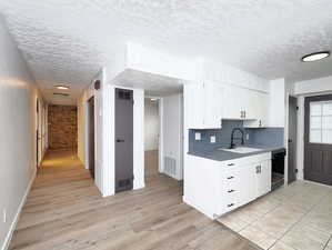 Unit #1- Kitchen with white cabinets, light wood-type flooring, dishwasher, a textured ceiling, and dark countertops