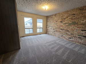 Unit #2- Unfurnished room with brick wall, carpet, and a textured ceiling