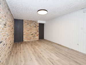 Unit #1- Empty room with light wood-style floors, brick wall, a textured ceiling, and wooden walls